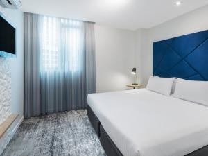 a bedroom with a large white bed and a window at Brady Apartment Hotel Flinders Street in Melbourne