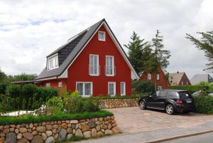 czerwony dom z czarnym samochodem zaparkowanym przed nim w obiekcie Ferienhaus Holst Sylt w mieście Wenningstedt