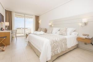 Un dormitorio con una gran cama blanca y una mesa en Landmar Playa La Arena, en Puerto de Santiago