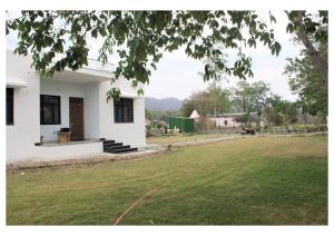 une maison blanche avec une pelouse verte devant elle dans l'établissement Kishkindha Wild 3BHK, à Rāmnagar