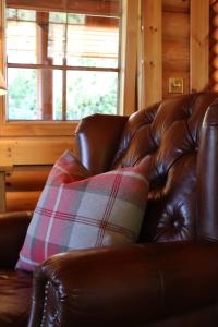 a brown leather couch with a plaid pillow on it at Bunnahahbain - Two Bedroom Luxury Log Cabin with Private Hot Tub in Berwick-Upon-Tweed