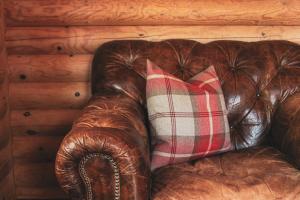 a brown leather couch with a plaid pillow on it at Tomatin - Luxury Two Bedroom Log Cabin with Hot Tub in Berwick-Upon-Tweed +11 photos