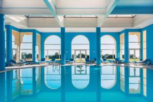 a swimming pool with chairs and tables in a building with windows at Iberostar Averroes in Hammamet