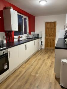 a kitchen with white cabinets and a wooden floor at The Superhost - 4 BR House in Sunderland