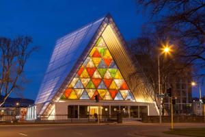 Ramada Suites by Wyndham Christchurch City في كرايستشيرش: مبنى بالواجهة الزجاجية الملونة في الليل