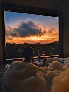 uma pessoa deitada na cama em frente a uma grande televisão em Chalés Mirante Monte Verde em Monte Verde