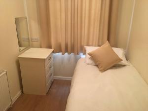 a small bedroom with a white bed and a dresser at Marios Lodge in Padstow