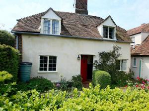 a white house with a red door and some bushes at Box Cottage in Eastling