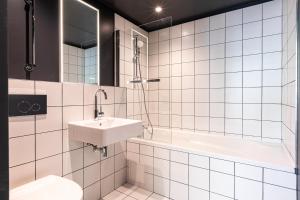 La salle de bains est pourvue de carrelage blanc, d'un lavabo et d'une baignoire. dans l'établissement Graphik Montparnasse, à Paris