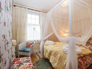 1 dormitorio con cama con dosel y silla en Bumble Bee Cottage, en Faversham