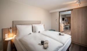 Un dormitorio con una gran cama blanca con zapatos. en elaya hotel oberhausen ehemals ANA Living Oberhausen by Arthotel ANA en Oberhausen