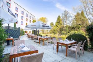 un patio con mesas, sillas y una sombrilla en elaya hotel frankfurt oberursel, en Oberursel