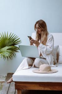 uma mulher sentada numa cama usando o seu telemóvel e um portátil em Neptune Studios Lombok em Kuta