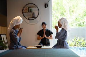 zwei Frauen sitzen an einem Tisch mit einer Frau im Spiegel in der Unterkunft Villoft Zen Living Resort in Thalang