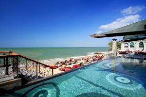a swimming pool next to a beach with people sitting in chairs at Pattaya Modus Beachfront Resort in North Pattaya