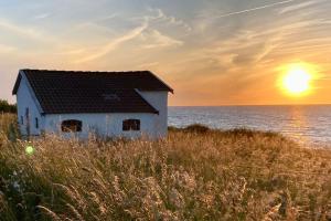 a house on the beach with the sunset in the background at Spacey and charming cabin 300 m. from beach in Tjørneholm