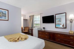 a hotel room with a bed and a dresser with a television at Travelodge by Wyndham Cape Cod Area in West Dennis