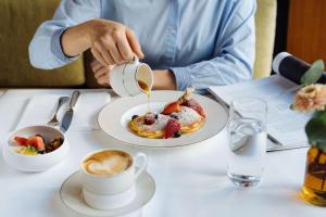 uma pessoa sentada numa mesa com um prato de panquecas e café em Park Hyatt Zurich – City Center Luxury em Zürich