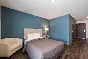 WoodSpring Suites Greensboro - High Point North في جرينسبورو: غرفة نوم زرقاء مع سرير وكرسي