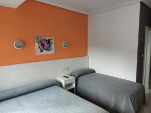 Habitación con 2 camas y pared de color naranja. en Hotel Cervantes, en Mahora