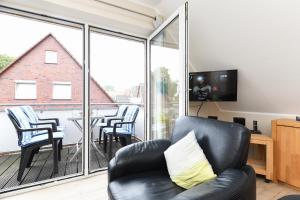 a living room with a black leather couch and a balcony at Ferienwohnung Langeoog Inselhaus am Deich in Neuharlingersiel
