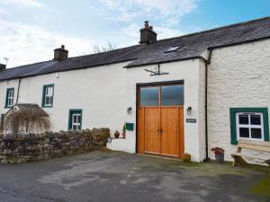 a white house with a wooden door and a bench at Keats Barn in Ireby