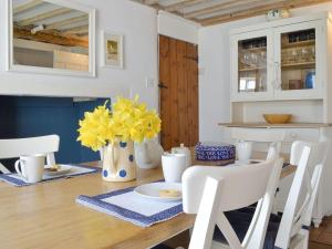 mesa de comedor con sillas blancas y flores amarillas en Apple Tree Cottage, en Foulsham