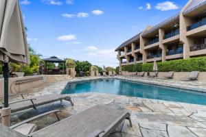 a swimming pool with chairs and a building at Kona Pacific A206 Condo in Kailua-Kona