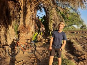 a man standing next to a bike next to a palm tree at Village Room in the Countryside in Al Minya