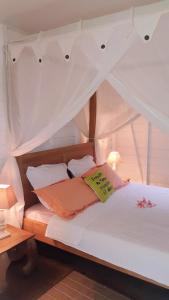 ein Schlafzimmer mit einem Himmelbett mit weißer Bettwäsche und Kissen in der Unterkunft Villa Gaïa - Bungalow Ti-Zen et son jacuzzi niché dans un jardin tropical, séjour en amoureux in Le Diamant