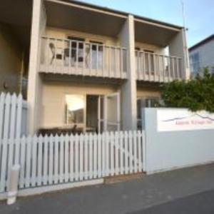 a white fence in front of a building with a dog on a balcony at La Voyageur Waterfront Apartments by AVI in Akaroa