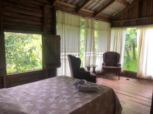 a bedroom with a bed and two chairs and windows at Santa Maria Volcano Lodge in Hacienda Santa María
