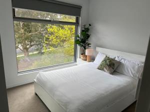 a white bed in a room with a large window at Centrepoint Units Heidelberg in Melbourne