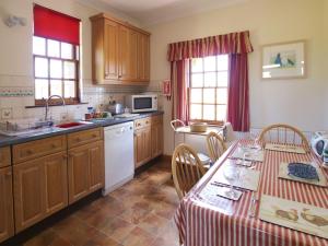 a kitchen with wooden cabinets and a table with chairs at Conheath Gatelodge Cottage in Kingholm Quay