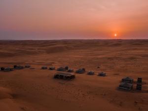 eine Gruppe von Fahrzeugen, die bei Sonnenuntergang in der Wüste geparkt sind in der Unterkunft Sands Dream Tourism Camp in Shāhiq