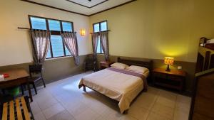 a bedroom with a bed and a desk and windows at Sepilok B&B in Sepilok