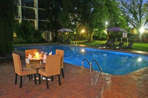 a table and chairs next to a swimming pool at night at Oudtshoorn Inn Hotel in Oudtshoorn