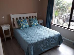 1 dormitorio con 1 cama con edredón azul y ventana en Sanlou, en Port Shepstone