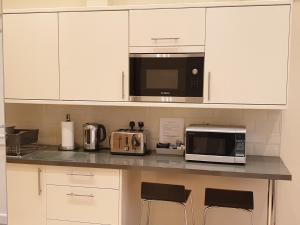 a kitchen with white cabinets and a microwave and some chairs at London Luxury Studio Flat 4 min to Ilford Station with FREE parking FREE WiFi in Ilford