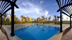 une grande piscine avec des palmiers et des maisons dans l'établissement Jaz Makadi Saraya Palms, à Hurghada