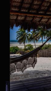a hammock on a beach with palm trees and the ocean at Villa Kabaceiras in Tatajuba