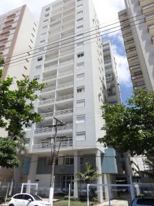 a tall white building with trees in front of it at Apartamento Pitangueiras in Guarujá