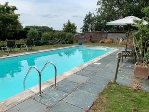 a swimming pool with chairs and an umbrella at Heron Barn in Hollingbourne