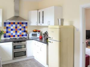  La cuisine est équipée de placards blancs et d'un réfrigérateur. dans l'établissement Curlew Cottage, à Creetown
