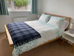a bed with a blue and white blanket and a window at 'Edgewood' - detached bungalow in Inverness
