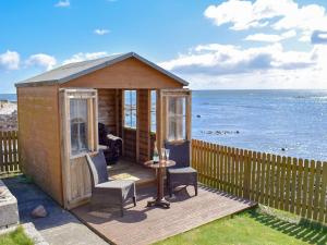 a wooden cabin with two chairs and a table and the ocean at Seashore Retreat in Johnshaven