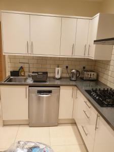a kitchen with white cabinets and a stainless steel dishwasher at London Luxury 1 bed flat 4 mins to Ilford Stn - kitchen, garden, parking, WiFi in Ilford
