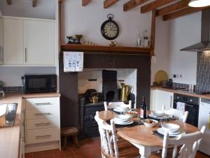 a kitchen with a wooden table with a clock on the wall at Bwthyn Pabi in Penmachno