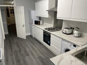a kitchen with white cabinets and a stove top oven at Modern 4 Bedroom House 10 mins from East Croydon with Garden and Free parking in South Norwood