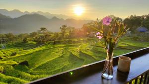 a vase with flowers on a balcony with a view of a field at Pu Luong May Home & Cafe in Làng Bang